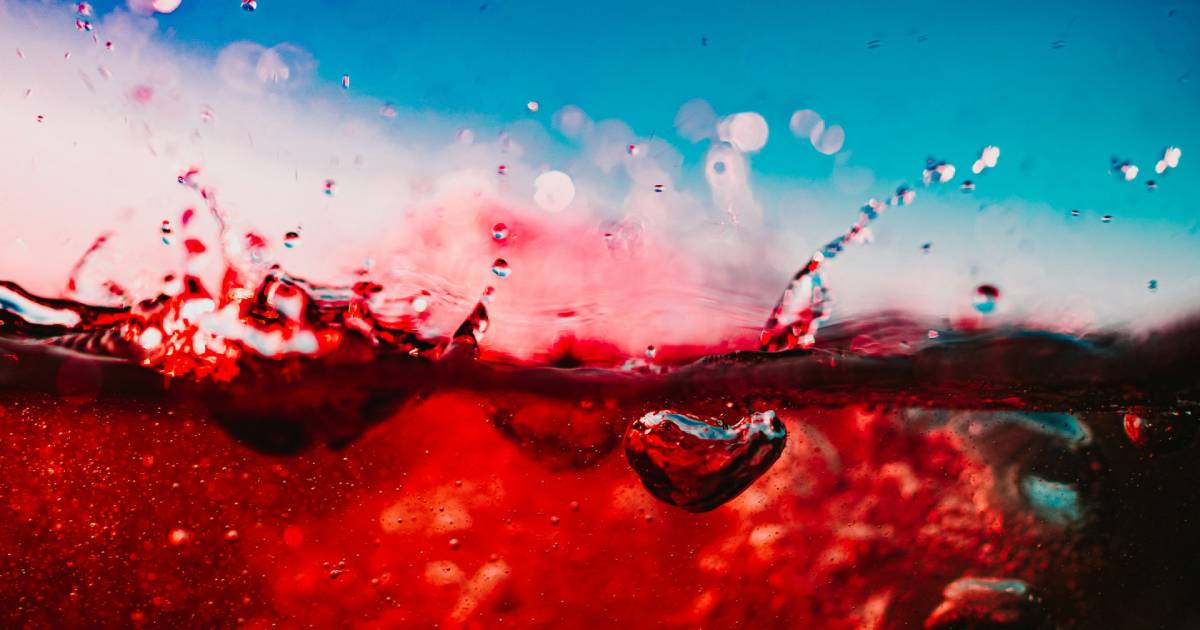 A glass of dark Zinfandel beside a spoonful of raspberry preserves on a weathered wooden table